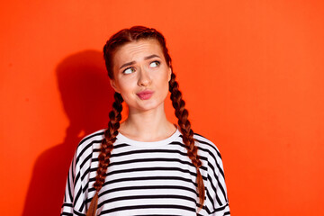 Charming young woman with red hair in striped pullover stands against vibrant orange background...