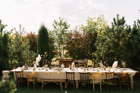 Long rustic wooden table set outdoors under greenery