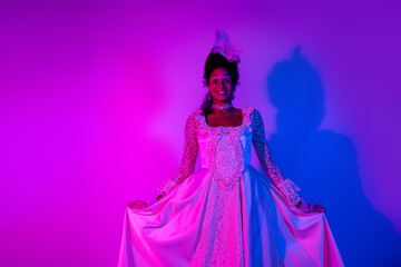 Elegant young woman in royal gown posing against vibrant pink and purple light