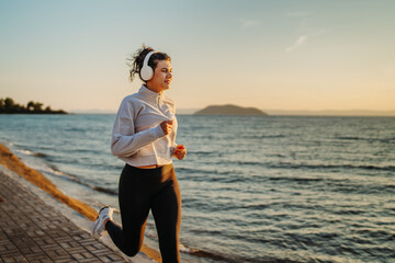 Young caucasian woman running or jogging on the beach at sunset	