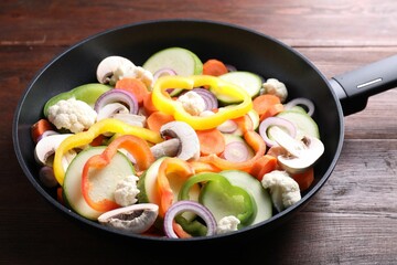 Frying pan with mix of vegetables and mushrooms on wooden table, closeup
