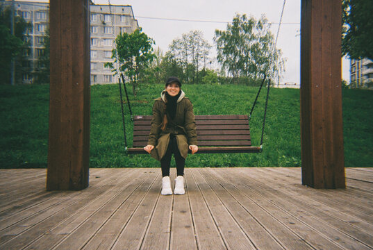Smiling woman sitting on a swing in a park in spring