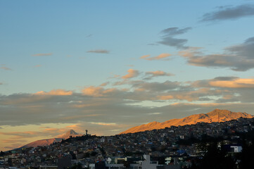 Fototapeta premium Silhouette of El Panecillo, the San Juan neighborhood and Toctiuco in the foreground. El Corazón hill in the background, in a golden sunrise.