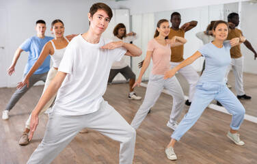 Fototapeta premium Group of sporty young adult multinational sports people making straight line with hands exercising dancing in gym