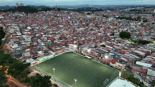 4k drone footage of a vibrant residential area in Osasco, Sao Paulo, Brazil, featuring a brightly lit soccer field in the middle of favela.