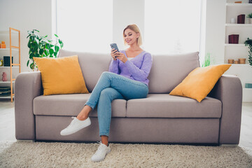 Young woman relaxing indoors while using smartphone in a bright living room, enjoying home comfort during the weekend