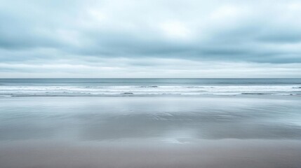 A tranquil beach scene with soft waves and overcast skies.