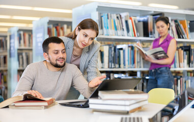 Guy and a girl students, preparing for the university library for the exam, are engaged on a laptop, discussing important ..issues of study