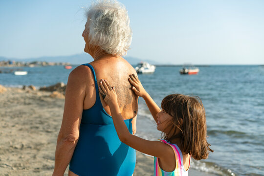 Little girl covering her grandmothers back with sand