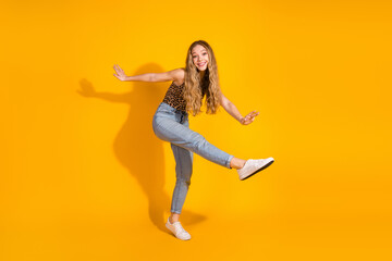 Obraz premium Energetic young woman poses playfully on a vibrant yellow background, showcasing fashionable style and joyful spirit