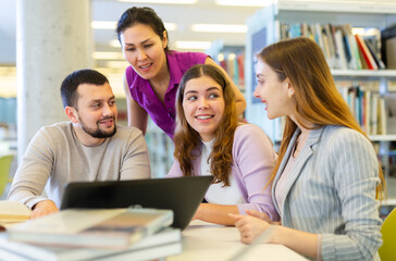 Friendly group of students studying in the university library is preparing for classes on a laptop, discussing current issues
