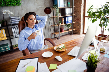 Fototapeta premium Confident young businesswoman enjoys a coffee break in a stylish office setting with elegant decor