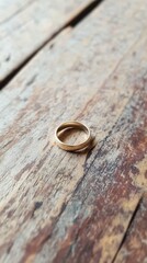 A simple gold ring resting on a weathered wooden surface.