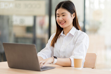 Obraz premium Portrait of a business asian woman sitting in an office with her colleagues in the background. Happy business woman working in a co-working office. 
