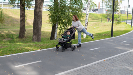 Obraz premium Caucasian woman roller skating with her toddler son in a stroller. 