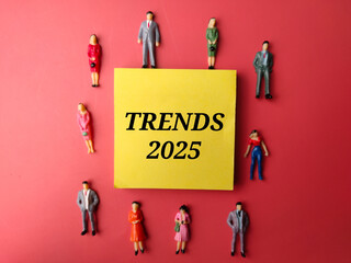 Miniature people and sticky note with text Trends 2025 on a red background. Business concept