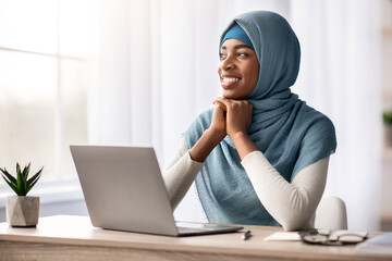 Portrait Of Pensive Happy Black Muslim Woman In Hijab Sitting At Desk With Laptop In Home Office, Islamic Lady Looking Away With Glad Face Expression, Thinking About Business Strategy, Copy Space