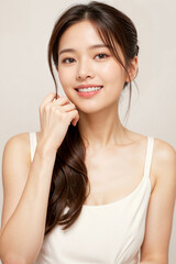 Naklejka premium Portrait of a Smiling Young Woman in Natural Soft Lighting Against a Neutral Background