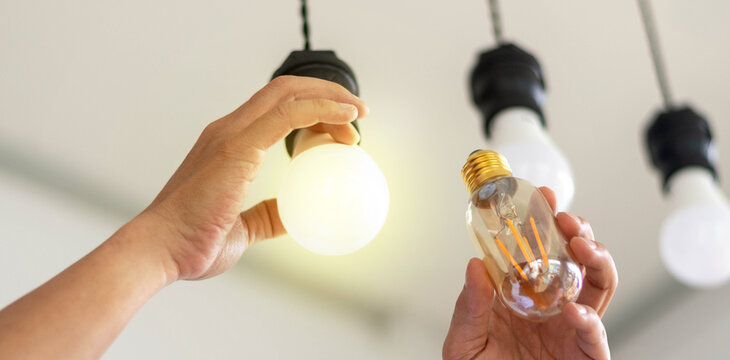 Power saving concept. Hands holding new Light Emitting Diode ( LED ) light bulb with light on and blur spiral compact-fluorescent (CFL) bulbs behind for copyspace.