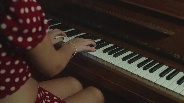Elegant and beautiful young female wearing an old-fashioned pois dress playing an old piano, and eventually smiling and winking at the camera