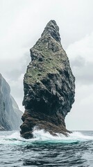 A tall, rocky formation rises from the ocean, surrounded by waves.