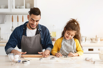 Positive Arab Family Dad And Daughter Baking Cookies In Kitchen Together, Cute Little Girl Cutting...