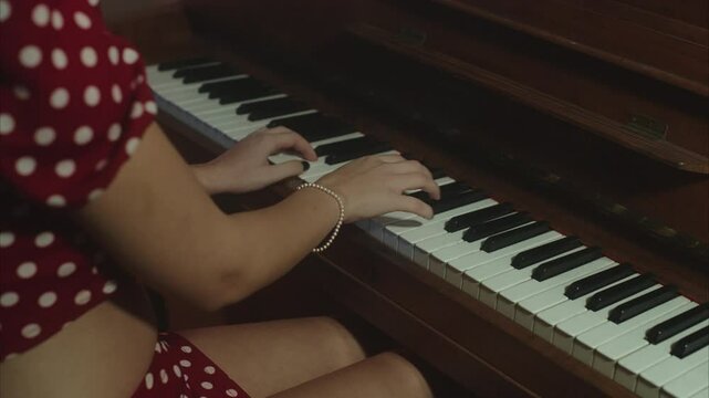 Elegant and beautiful female artist wearing an old-fashioned pois dress playing an old upright piano, and then watching suspiciously at the camera while sensually tickling her hair
