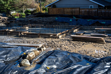 Residential construction start, foundation dug and cement pour forms started with wood and rebar, wet and buddy job site on a sunny winter day
