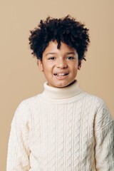 Portrait of a young african american boy in a white turtleneck sweater against a soft beige background