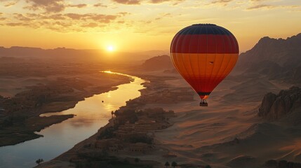 Obraz premium Hot air balloon floating over serene deserts with a river, capturing the beauty of dawn with dramatic colors and tranquil landscapes in a breathtaking aerial view