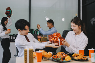 full length view of a group of business team wearing red Santa hat and exchange gift box together in the office for Christmas.