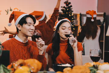 Group of young Asian man and women as friends having fun at a New Year's celebration, holding gift boxes standing by Christmas tree decoration, midnight countdown Party at home with holiday season.