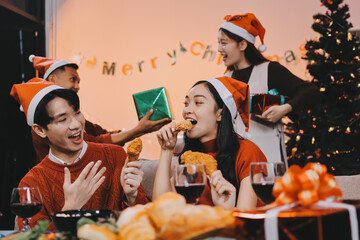 Group of young Asian man and women as friends having fun at a New Year's celebration, holding gift boxes standing by Christmas tree decoration, midnight countdown Party at home with holiday season.