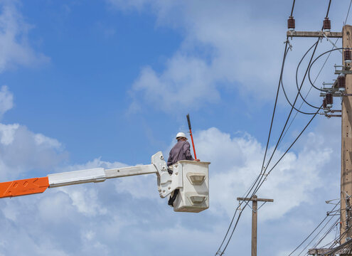  lineworker in bucket hydraulic lifting platform while electrical installation and repairs the power line on electricity power pole under blue sky