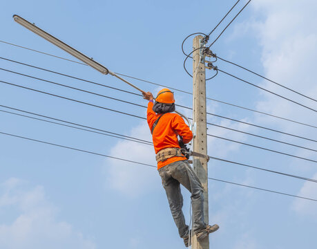   Electrician lineworker climb work installing new street lamp on electricity power concrete pole in construction site under blue sky    