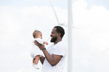 African American father embracing and carrying newborn baby outdoor at windmill field farm on holiday travel. Happy father and newborn playing together outdoor