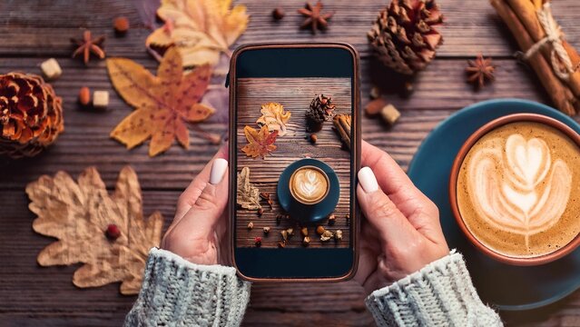 photography blogging workshop concept. hand holding phone taking photo of stylish winter flat lay coffee cookies and spices on wooden rustic background. cozy mood autumn.