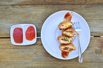 Top view of mayo risoles with fork on the white plate. Isolated on the wooden table. Tomato and chilly sauce on the left