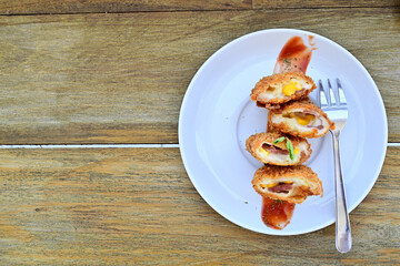 Top view of mayo risoles with fork on the white plate. Isolated on the wooden table. Free space, copy space, empty space on the left side.