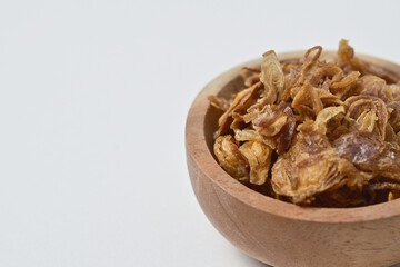 Half view of Indonesian crispy deep fried shallots or onion flakes (bawang goreng) in a wooden small bowl. Isolated on the white background. Copy space, empty space, free space, close up view.