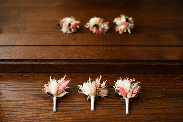 3 boutonnieres on a wooden surface, made of dried flowers and herbs, white and pink.