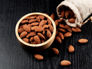 Almonds in a wooden bowl on a black wooden background with space for text. The food is ready to be eaten as a snack or used as an ingredient for baking.