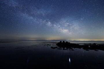 海の水面にゆれる星と天の川と能登半島の星空