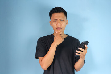 Young Asian man thinking about something while holding his mobile phone