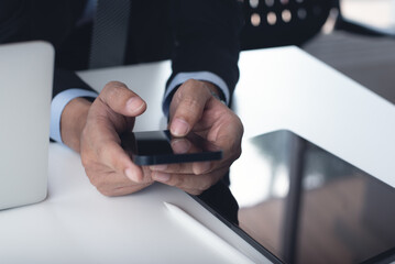 Businessman in black suit using mobile phone during working at office with digital tablet and laptop computer on table, close up. Business man surfing the internet at workplace