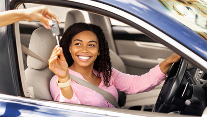 Car Sales. Manager giving new auto key to happy young black lady at dealership store, selective...