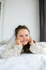 A young woman with Down syndrome lies on a bed, smiling serenely. Her relaxed pose and gentle expression convey a sense of peace and contentment