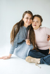 A cheerful mother and daughter with Down syndrome sit together on a white background, their happy...