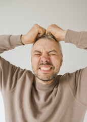 Obraz premium Close-up portrait of a man clutching his hair in frustration or anger. His face is contorted in a grimace, eyes squeezed shut, expressing intense negative emotion. 