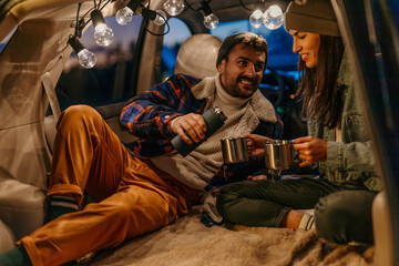 Man and woman sharing hot beverages in a car trunk setup